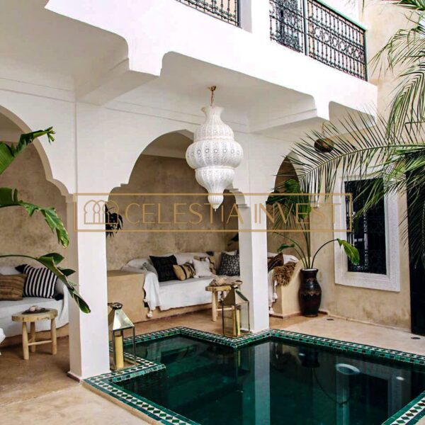 Elegante riad de diseño tradicional marroquí, con piscina cubierta de mosaicos verdes, arcos blancos y cómodos asientos.