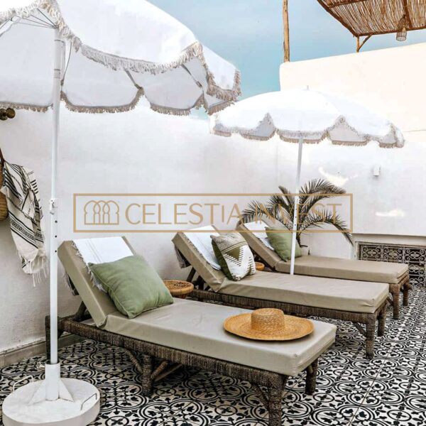 Terrasse sur le toit d'un riad avec des chaises longues élégantes sous des parasols blancs à franges, des carreaux à motifs et une vue sur la ligne d'horizon de Marrakech.