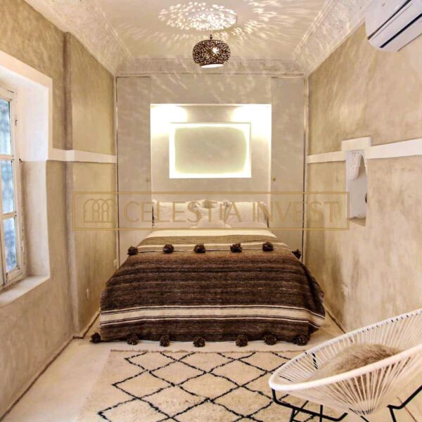 Chambre à coucher confortable du Riad avec des murs rustiques en tadelakt, un lit confortable avec des textiles marocains traditionnels et une lampe suspendue chic qui projette des motifs au plafond.