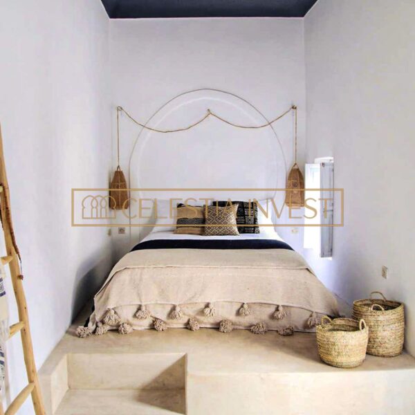 Chambre à coucher minimaliste du Riad avec un lit surélevé, un décor en fibres naturelles et des murs blancs simples créant une atmosphère sereine.