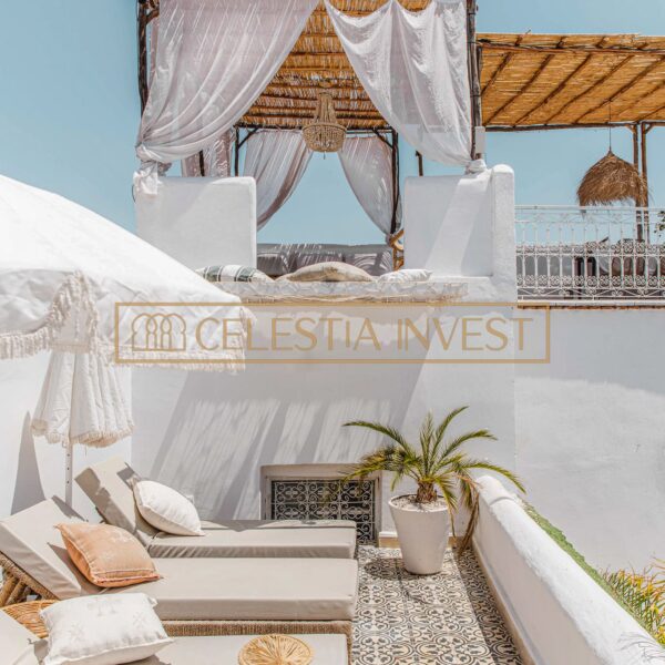 Terrasse de Riad avec banquettes et rideaux blancs flottants, structure en rotin et carrelage à motifs