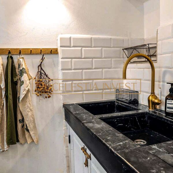 Cocina del Riad con fregadero de mármol negro, grifos dorados, azulejos blancos y paños de cocina colgantes.