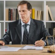 Un homme d'âge mûr travaillant sur un ordinateur portable tout en examinant un document dans un bureau de style juridique.